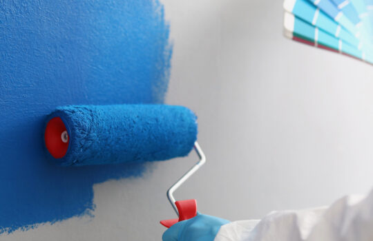 Painter with brush tool covered in blue colour painting wall, worker on site